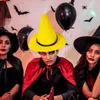 Three people in Halloween costumes posing for a photo with balloons and decorations in the background. Produktbild-Vorschau