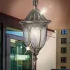 An outdoor pendant light fixture hanging from a ceiling, with a building visible in the background. Náhled obrázku produktu