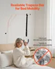 A woman is sitting on a bed and holding onto a trapeze bar attached to the bed frame. Náhled obrázku produktu