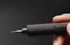 A hand holds a dark gray electric screwdriver with a bit attached. Náhled obrázku produktu