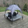 A black dog is resting on an elevated dog bed with a canopy, outdoors on a wooden deck. Produktbild-Vorschau