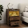 A wooden nightstand with two drawers and an open shelf, placed next to a bed. The nightstand has a lamp, a book, a clock, and a small elephant figurine on it. Produktbild-Vorschau