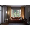 A living room scene with a sofa, window, and a wall lamp. Produktbild-Vorschau