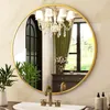 A round gold-framed mirror is mounted above a sink in a bathroom, reflecting a chandelier, curtains, and a dresser. Produktbild-Vorschau