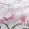 A close-up view of a white sheer curtain with a floral pattern and text visible underneath. Produktbild-Vorschau