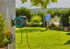 A man is watering a garden with a hose reel mounted on a wall. Voir les images du produit