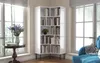 A white corner bookshelf filled with books is placed next to a window with a blue sofa in the foreground. Produktbild-Vorschau