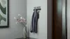 A hallway scene with a coat rack, a vase of flowers, and a framed picture. Náhľad obrázku produktu