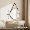 A round mirror with a black strap hangs above a wooden vanity in a bedroom setting. Voir les images du produit