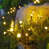 Solar-powered firefly lights illuminating a garden at dusk. Produktbild-Vorschau