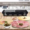A raclette grill with various food items like cheese, meat, pickles, and bread arranged around it on a wooden table. Produktbild-Vorschau