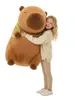 A young girl hugging a large plush capybara toy. Produktbild-Vorschau