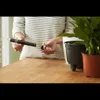 A person is holding a plant watering device next to a potted plant. Produktbild-Vorschau