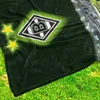 A dark green blanket with the Borussia Mönchengladbach logo and two yellow stars, laid out on a grassy surface, with a stadium view in the background. Produktbild-Vorschau