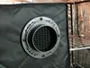 Close-up of a ventilation baffle with a grid inside, attached to a black fabric surface. The background shows a reflective interior and a metal shelf. Produktbild-Vorschau