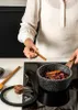 A person is cooking in a kitchen, adding spices to a pot on a stovetop. Produktbild-Vorschau