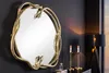 A decorative mirror with a snake-shaped frame is displayed on a dark wall, with two lit candles and a lamp in the background. Produktbild-Vorschau