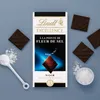 A chocolate bar and pieces of chocolate are arranged with sea salt on a gray surface. Produktbild-Vorschau