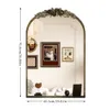 A decorative arched mirror with a floral motif at the top, reflecting a room with several framed pictures and furniture. Podgląd zdjęcia produktu