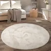 A round, fluffy rug is placed on a wooden floor in a living room setting, with a sofa and side table in the background. Produktbild-Vorschau