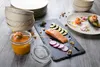 A table setting with a slate serving platter featuring salmon, avocado, and radishes, alongside a jar of soup and stacked bowls. Produktbild-Vorschau