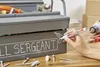 A person is writing on a toolbox with a marker. Tools and screws are scattered around the toolbox. Produktbild-Vorschau