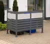 A metal bin enclosure for trash cans is shown outdoors on a paved patio, next to a building and some greenery. Náhled obrázku produktu