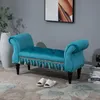 A teal upholstered bench with decorative tassels sits on a patterned rug in a room with gray walls. A tall white vase and a framed picture are visible in the background. Produktbild-Vorschau