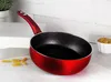 A red frying pan with a black interior sits on a white countertop, with some uncooked pasta in the foreground and a small bowl of cooked pasta in the background. Produktbild-Vorschau