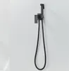 A black bidet sprayer and hose mounted on a white wall. Náhľad obrázku produktu