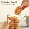 A hand is taking a cookie from a stack of cookies inside a glass jar, with a mug in the background. Produktbild-Vorschau