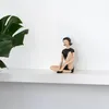 A decorative figurine of a woman in a vintage swimsuit sitting on a shelf next to a plant. Anteprima dell’immagine prodotto