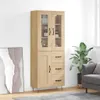 A tall, narrow wooden cabinet with glass doors and drawers, standing in a room next to a large plant and a framed picture. Podgląd zdjęcia produktu