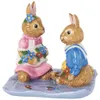 Two ceramic bunnies sitting on a blue checkered mat with flowers. Náhled obrázku produktu