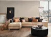 A living room scene featuring a sectional sofa, ottoman, and decorative items, with a city view through a large window. Produktbild-Vorschau
