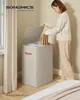 A woman is putting laundry into a two-compartment laundry basket in a bedroom setting. Produktbild-Vorschau