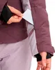 A person's hand is shown inserting a card into the zippered pocket of a purple and light purple ski jacket. Produktbild-Vorschau