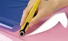A hand is using a yellow rotary cutter to cut through pink fabric, with a blue sheet of material visible in the background. Náhled obrázku produktu