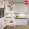 A woman is standing on a step stool in a modern kitchen, reaching for a glass on a high shelf. Anteprima dell’immagine prodotto