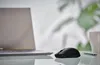 A black computer mouse is placed on a reflective surface next to a laptop. Voir les images du produit