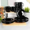 A collection of black dinnerware, including plates and bowls, is displayed on a wooden cutting board and a shelf. Podgląd zdjęcia produktu
