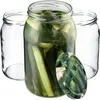 Three glass jars, one filled with pickles and brine, and two empty jars are arranged on a white background. A lid with a pickle pattern is placed in front of the filled jar. Podgląd zdjęcia produktu