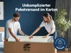 A couple is unboxing a rolled-up mattress from a large cardboard box. Produktbild-Vorschau
