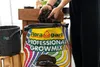 A person is shown adding soil from a wooden box into a large bag of "Floragard Professional Growmix". A fabric grow bag is visible to the left. Produktbild-Vorschau