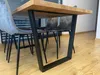 A close-up view of a dining table with black metal legs and a wooden top, surrounded by gray upholstered chairs. Anteprima dell’immagine prodotto