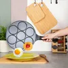 A hand holding a pancake pan with pancakes and an egg being cooked, with a plate and utensils on a kitchen counter. Produktbild-Vorschau