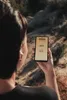 A person is holding a smartphone outdoors, with a natural landscape in the background. Anteprima dell’immagine prodotto