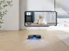 A robot vacuum cleaner is shown on a wooden floor, with a smartphone displaying a live feed of a cat. The smartphone is held by a hand outline, suggesting remote control. Produktbild-Vorschau