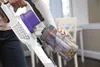 A person is holding a cordless vacuum cleaner and detaching the dustbin. Podgląd zdjęcia produktu
