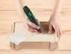 Hands using a cordless engraving tool to decorate a wooden box, with stencils nearby. Produktbild-Vorschau